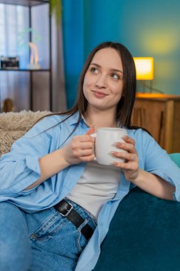 Evdeki genç bayan rahat bir şekilde kanepede oturuyor, elinde sıcak bir fincan çay ya da kahve tutuyor, sakin bir sabahın tadını çıkarıyor. Kafkas kızı huzuru, sessizliği ve hoş kokulu içecek ayinini takdir ediyor.