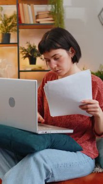 Kanepede dizüstü bilgisayarını kullanarak evrak işleriyle uğraşan beyaz, genç bir kadın. Gayri resmi giyinmiş, bağırarak dokümanları hava kapatma ağına atan ve evdeki oturma odasına bakan üzgün bir kız.