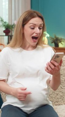 Hamile, orta yaşlı bir kadın akıllı telefondan bebek kıyafetlerinin satışını görüyor. Büyük tasarruf yaparken gözleri parlıyor. Kanepede alışveriş yapan bir kız annelik kıyafetlerini hayal ederek indirimi kutluyor..