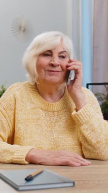 Telefon, iyi haber, dedikodu. Akıllı telefondaki hoş sohbetimizde son sınıf öğrencisi mutlu bir sürpriz oldu. Evde arkadaşınla konuşmaktan keyif alıyor. Yaşlı olgun büyükanne masada koltukta oturuyor..