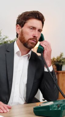 Merkez ofisteki orta yaşlı işadamı eski telefonlara cevap veriyor ve müşteriyle konuşuyor. Masadaki serbest çalışan adam yardım notları sunuyor ve yardım hattı desteği için sakin bir tonda devam ediyor.