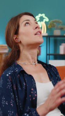 Gergin, beyaz bir kadın evdeki kanepede oturup avuç içlerini birleştirir. Yardım dileyin. Stresli hissedin. Endişeli genç kız dua ediyor dilek diliyor özür diliyor