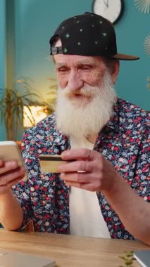 Merkez ofisteki online alışveriş ödemeleri için banka kartı ve dizüstü bilgisayar kullanan Kafkasyalı kıdemli bir adam. İş anlaşması. Gülümseyen şık büyükbaba satın alımları netbook E-bankacılık uygulama hizmeti ile.