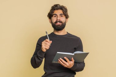 Düşünceli genç Hintli iş adamı not alıyor, not defterine kalemle düşünceler yazıyor, liste yapmak için, iyi fikir. Arap yetişkin adam bej renkli stüdyo arka planında izole edilmiş.