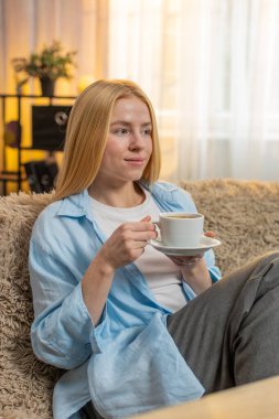 Evde sıcak kahve içen bir kadın, yavaşça yudumlarken gözlerini kapayan bir kadın. Kanepede oturan bir kız canlanıyor. Sessizlikten keyif alıyor. Sabahın erken saatlerinde pozitif havayla harmanlıyor.