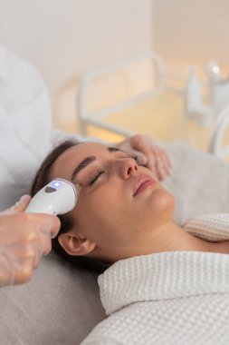 Kozmetik uzmanı, kadını yüz ve yanak bölgesinin kaldırma prosedürü, kolajen maskesi yapar. Güzellik uzmanı vakumlu yüz masajı terapisi için elektrikli ekipman kullanıyor. Cilt bakımı güzellik tedavisi. Dikey çekim