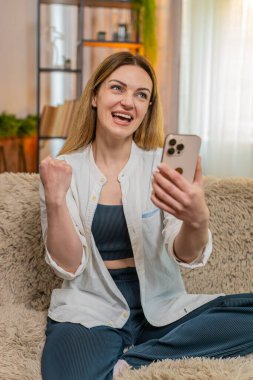 Orta yaşlı bir kadın internet üzerinden ikramiye kazandığını öğrenince sevinçten gülümseyen akıllı telefonları kontrol ediyor. Genç yetişkin kız hareketli zaferi kutluyor, başarıyla mutlu ve mutlu hissediyor.