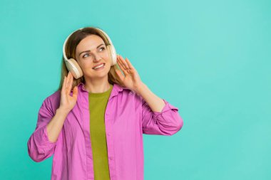 Orta yaşlı bir kadın kablosuz kulaklık takar ve hafif dans hareketleriyle ritim tutturmaya başlar. Mavi arka planda izole edilmiş bir kız, sevincini ve enerjisini favori sesleri dinleyerek gösteriyor.