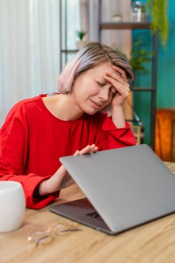 Genç bir kadın, dizüstü bilgisayarını evde oturmuş uzun bir çalışmadan sonra başını tutarak şiddetli bir baş ağrısı gösteriyor. Kafkasyalı kız yorgun, uzak çalışma yorgunluğundan rahatsızlık ve acı çekiyor..