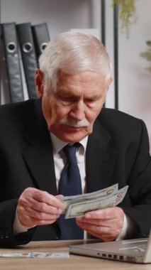 Diz üstü bilgisayarda çalışan zengin bir büyükbaba işadamı nakit para sayıyor, iş yerindeki gelir gelirlerini hesaplıyor. Profesyonel serbest meslek sahibi. İş adamları. İstihdam mesleği