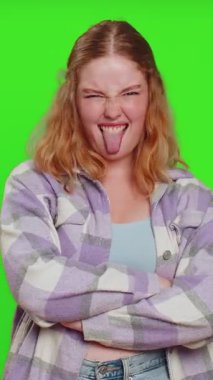 Komik, şakacı, genç bir kadın aptalca yüz ifadeleri takınıyor, suratını buruşturuyor, etrafta takılıyor, dil gösteriyor, aptalca bir ifade sergiliyor. Yeşil krom anahtar arka planında izole edilmiş bir kız. İnsan yaşam tarzları