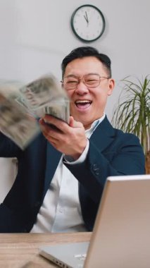 Orta yaşlı mutlu Asyalı işadamı, piyango kazanan piyango talihlisi, laptopta çalışırken kazandığı parayı paylaşarak para harcıyor. Çinli adam.