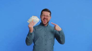 Zengin, mutlu, orta yaşlı, gözlüklü, mutlu bir beyaz adam elinde para, euro nakit para, hayran gibi banknotlar, başarılı iş kariyeri, piyango talihlisi, büyük gelir kaynağı. Mavi arkaplanda izole edilmiş adam