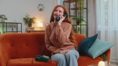 Gülümseyen genç bir kadın evdeki kanepede oturan arkadaşlarıyla telgraflı telefon konuşması yapıyor. Mutlu, heyecanlı kızıl kız 90 'lardan kalma eski moda telefondan keyif alıyor oturma odasında konuşuyor..