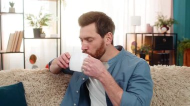 Evdeki adam kanepede oturup dinleniyor, sabahları elinde bir fincan sıcak çay tutarak düşünceli bir şekilde uzaktan bakıyor. Adam huzurlu bir andan hoşlanıyor, rahatlamış hissediyor, muhtemelen derin düşüncelere dalmış.