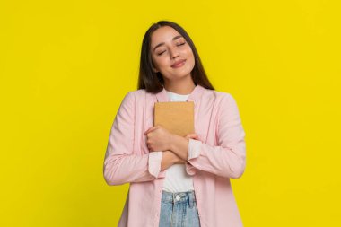 Genç kadın nazikçe gülümsüyor, kitabı kapatıyor okuduktan sonra tatmin edici bir duygusal tepkiyle göğsüne bastırıyor. Sarı arka plandaki kız sıcaklığını ifade eder. Yürekten hikâyeye dokunmanın verdiği neşe.