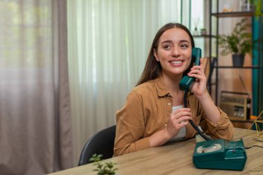 Masadaki genç kadın 90 'lardan kalma telefonları elinde tutuyor ve neşeli sohbetler sırasında yüksek sesle gülüyor. Kafkasyalı kız eğlenceli geçmişe dönük tarzdan hoşlanıyor ve neşeli konuşmalar yaparak parlak enerjisini ifade ediyor.