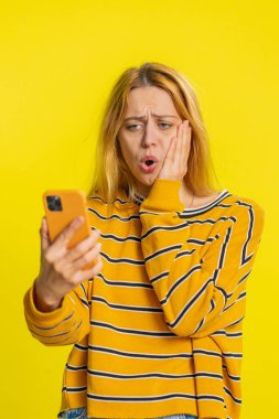 Üzgün beyaz kadın akıllı telefon daktilo kullanıyor, oyun oynuyor, aniden piyango sonucuna şaşırıyor kötü şans kaybı şanssız haber. Sarı arka planda izole edilmiş mutsuz, çekici kız.
