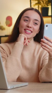 Beyaz bir kadın akıllı telefonuyla selfie çekiyor abonelerle internetten iletişim kuruyor sosyal medya için vlog hikayeleri kaydediyor. Masada ev ofisinde oturan kadın.