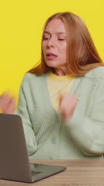 Mutlu Kafkasyalı orta yaşlı iş kadını dizüstü bilgisayar üzerinde çalışıyor zaferin şokunu kutluyor gol başarısını kutluyor, iyi e-posta kariyeri haberleri sarı arka planda yalnız başına oturuyor.