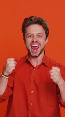 Mutlu beyaz adam başarıyı kutluyor zaferi, doğum gününü, piyango hedefini başarıyı iyi haber zaferini. Genç yakışıklı adam turuncu stüdyo geçmişinde izole edilmiş.