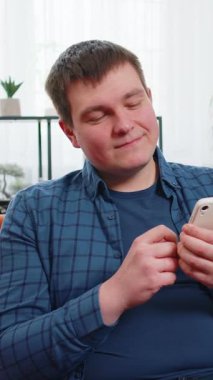 Gündelik giysiler içinde yukarı bakıp akıllı telefondan mesaj atan genç bir adam. Beyaz adam kanepede oturuyor ve evdeki oturma odasında cep telefonu kullanıyor. Erkek, dairede online film izliyor..