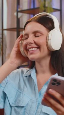 Kanepede oturmuş, kablosuz kulaklıkla müzik dinleyen neşeli genç bir kadın. Evde müzik eşliğinde dans eden sıradan giyinmiş neşeli yetişkin bir kız. Dans müziğinin tadını çıkarıyorum. Yaşam Tarzları