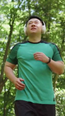 Sporcu spor koşucusu maraton koşusu yapıyor, kulaklıkla müzik dinliyor. Sabah parkta kardiyo çalışması var. Asyalı genç adam sağlıklı yaşam tarzını seviyor. Aktif sporcu koşucu.