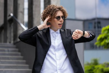 Kafkasyalı genç işadamı kol saatine bakıyor. Şok gecikmesi daha hızlı gidiyor. İşvereni binanın yakınındaki açık havada geziyor. Takım elbiseli, kıvırcık saçlı yakışıklı adam..