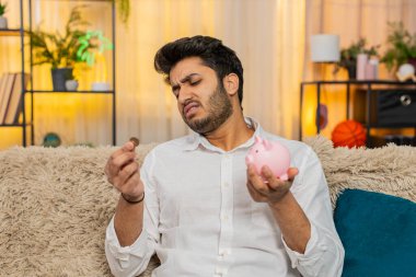 Evde oturan Hintli adam içi bozuk para dolu boş kumbaraya bakıyor, hayal kırıklığına uğramış hissediyor. Kanepede oturan Arap adam mali zorluklarla boğuşuyor ve zor bir durumla karşı karşıya. İflas