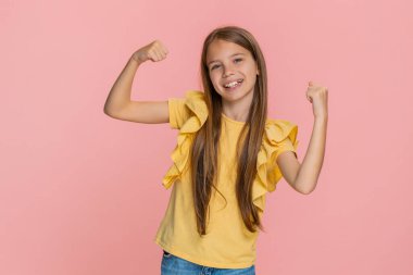 Genç kız zafer kazanarak elini kaldırıyor. Parlak bir gülümseme ve neşeli bir başarı anını kutluyor. Pembe arka planda izole edilmiş, neşeli enerji ve olumlu duygularla dolu bir okul çocuğu.