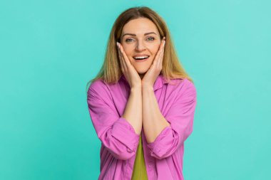 Orta yaşlı bir kadın yüzünü iki eliyle kapatıyor. Ani bir olaya şok, sürpriz ve inançsızlıkla tepki veriyor. Mavi arka planda izole edilmiş genç bir kız güçlü bir duygusal tepki gösteriyor