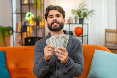 Evdeki Hintli adam dolar sayıyor nakit para, seyahat bütçesi gülücük planlarını nereye koyacağını düşünüyor. Kanepede para taşıyan Arap bir adam yolculuk hayalleri kuruyor.