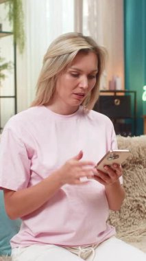 Yenilgide online oyun omuzlarını kaybettikten sonra evde oturup akıllı telefon kullanan hamile bir orta yaşlı kadın. Kanepedeki beyaz kız üzgün yüzünü gösteriyor. Titreyen kafa cep telefonu ekranına bakıyor ve üzgün hissediyor..