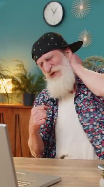 Son moda gömlek ve şapkalı yaşlı sakallı adam dizüstü bilgisayara bakıyor ve boynundan ve sırt ağrısından muzdarip bir şekilde masada otururken dans ediyor. Yaşlı büyükbaba işyerinden izin alıyor..