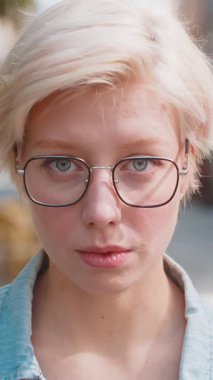 Mutlu genç kadın yüzünün yakın plan portresi gülümseyen dostça bir gülümseme, dinlenme kamerasına bakmak dışarıda iyi haberler veriyor. Şehir caddesinde kısa sarı saçlı, gözlüklü güzel bir yetişkin kadın..