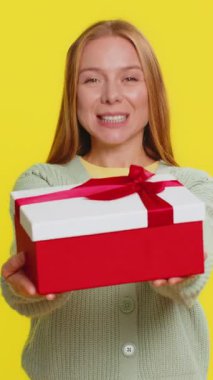 Olumlu gülümseyen olgun bir kadın doğum günü hediyesi paketini sunar, hediye paketini uzatır, hediye ikramiyesi sunar, parti promosyonu indirimini kutlar Noel indirimini kutlar. Sarı arka plandaki kız