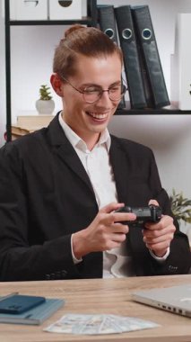 Kafkasyalı genç iş adamı laptopta video oyunu oynuyor, boş zamanlarını ofis masasında geçiriyor. Mola sırasında joystick kontrolörüyle video oyunu oynayan mutlu stil sahibi serbest yazar..