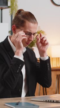 Yorgun ve genç bir iş adamı. Gözlüklerini çıkarıyor. Kuru gözlere masaj yapıyor. Ofiste dizüstü bilgisayar kullandıktan sonra aşırı çalışan adam göz yorgunluğu çekiyor. Baş ağrısı, görsel yorgunluk ve göz ağrısı konsepti.