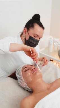 Kozmetik uzmanı, beyaz bir kadının özel nemlendirici kremini sürüyor, yüzünü ovuyor, soyuyordu. Güzellik salonunda yüz bakımı yaşlanmayı önleyen kozmetik masaj prosedürü. Güzellik tedavisi. Dikey