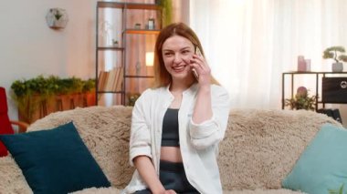 Orta yaşlı bir kadın evde akıllı telefonuyla konuşuyor, samimi bir şekilde gülüyor ve el hareketini açıklık ve neşe göstermek için kullanıyor. Genç yetişkin kız, sıcak ve duygusal bağlarını ifade ederek keyifli sohbetlerden hoşlanır..