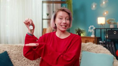 Evdeki koltukta anahtarı tutan mutlu genç bir kadın başarılı bir alımı ya da taşınmayı mutlulukla kutluyor. Beyaz kız heyecanla gülümsüyor, neşeli ev sahibi jesti, gayrimenkul başarısı gösteriyor.