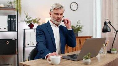 Merkez ofisteki orta yaşlı gülen işadamı laptopla yardım hattını arayan kişiye kulaklık takıyor. Masadaki serbest çalışan müşteri memnuniyetini artırmak için hızlı destek veriyor.