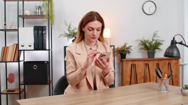 Merkez ofisteki orta yaşlı iş kadını akıllı telefon banka başvurularının faturalarını ödüyor ödemeler tamam işaret gülümsemeleri ve rahatlama. Masadaki serbest çalışan kız online ödeme bütçesi onaylama kartı başarısını yönetiyor.