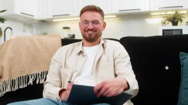 Evdeki genç adam not defterine günlük plan çizer öncelikleri belirler ve görevler için basit bir program yazar. Kanepede oturan beyaz adam hedefleri sıralıyor zaman blokları ekliyor ve sakin bir ruh hali ve berrak bir zihinle odaklanıyor..