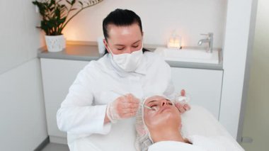 Enzim terapisi. Güzellik uzmanı orta yaşlı bir kadının yüzüne fırçayla nemlendirici kimyasal krem maske takıyor. Yetişkin kız cilt bakımı prosedürü. Yüz kozmetolojisi tedavisi.