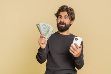 Lübnanlı genç adam akıllı telefonu samimi bir şekilde neşeyle kazanıyor, para dolar banknotları alıyor, piyango talihi, gelir maaşı alıyor. Stüdyo bej arka planda Hintli adam..