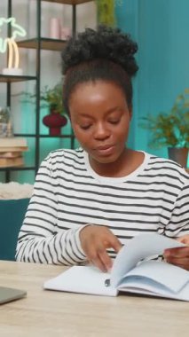 Evde çalışan Afro-Amerikalı siyahi kadın. Genç kız kanepede dizüstü bilgisayar kullanarak oturuyor, not defterine notlar yazıyor. Oturma odası düzeni, odaklanmış ifade, gevşemiş atmosfer, üretkenlik.