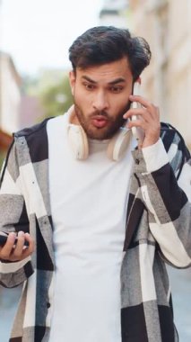 Sinirli, stresli Hintli genç adam, iki cep telefonuyla bağırarak konuşuyor. Sohbet ediyor, kavga ediyor, şikayet ediyor, sorunları dışarıda çözüyor. Şehir sokağındaki adam..