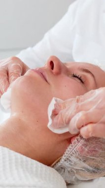 Klinikteki güzellik uzmanı kozmetikçi kadın yüzünden yumuşak süngerlerle nazikçe maske temizliyor. Profesyonel yüz bakımı enzim veya kimyasal peeling işleminden sonra tedaviyi temizler.